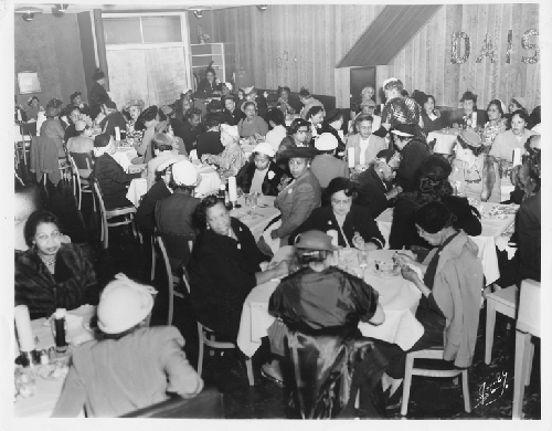 Women seated at white-cloth covered tables in Slim Jenkins Bar and Restaurant with letters 'Daisy Bridge Club' fixed to paneled wall in background