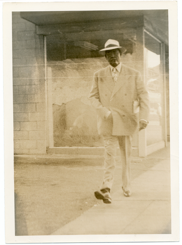 Slim Jenkins dressed in suit, tie, and white hat walking down sidewalk