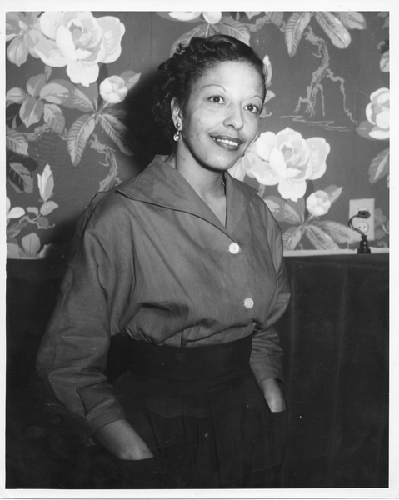 Unidentified woman stands against wallpapered background
