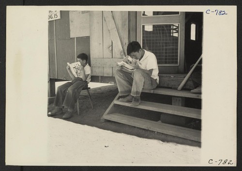 Manzanar, Calif.--Evacuee boys of Japanese ancestry at entrance of Recreational Hall reading Funnies. Photographer: Lange, Dorothea Manzanar, California