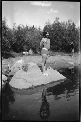 Girl in swim suit standing on boulder next to water