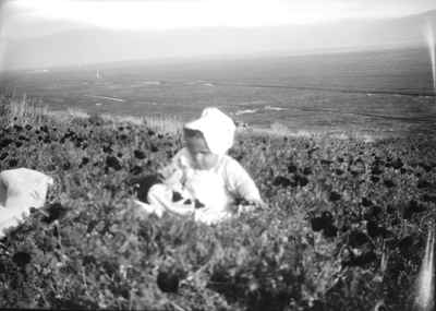 Baby wearing a bonnet sitting on cliff by the ocean