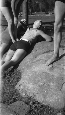 Two women in swim suits and caps lying on rocks