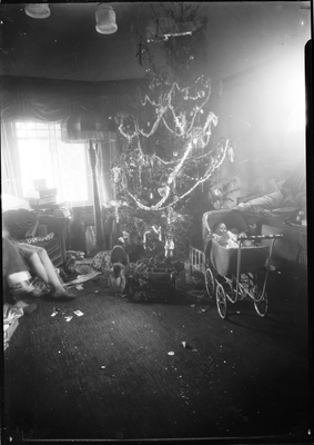 Baby in carriage in living room next to Christmas tree