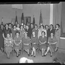 A group of women seated and standing in front of flags
