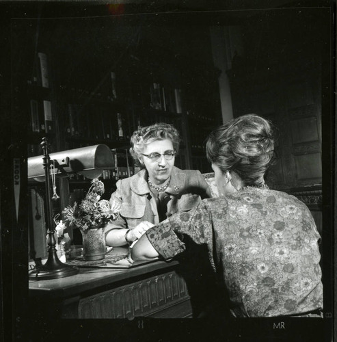 Dorothy Drake and a student converse at a desk in Denison Library, Scripps College