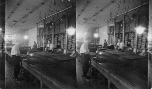 Cutting pants by hand (electric machine) 10 to 20 layers of cloth - at left the machine has a round (wheel) knife - at right machine has a vertical knife which goes up & down. N.Y. City