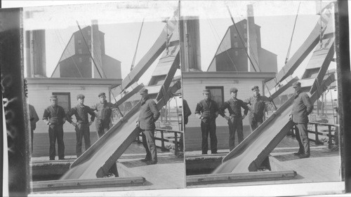 Loading steamers with wheat from elevators. Fort Willam, Ontario, Canada