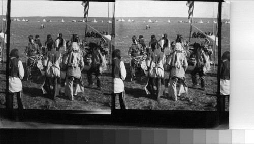 Grass Dancers in action. The Tom Tom beaters and singers being in the Shade of the Canopy. Fort Belknap Reservation, Mont., July 1906