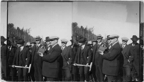 Gov. Bone holding gold Spike, Chairman Joe Steere. Alaska R.R. holding sledge hammer. Hoover in rear Bone. Work between Bone and Steere. Scene at end of Tetana Bridge at Nenana, Alaska