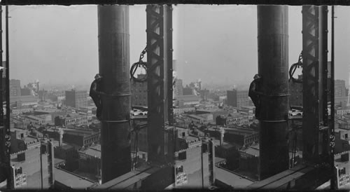 Clinging by hands and toes - steel worker finishing a big smokestack, New York