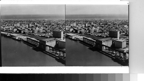 Air view of Galveston, Texas. Picture is taken looking from docks on Galveston Bay across Galveston Island to the Gulf of Mexico in background. In foreground are grain elevators of Galveston wharves, principal origin of greatest gulf grain export cargoes