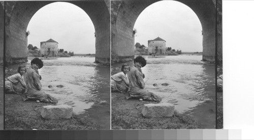 Two little Spanish girls use the Guadalquivir for washing the clothes. bridge of Guad. [Guadalquivir] Arch frames the Moorish tower. Cordoba, Spain