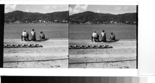 Island of St. Thomas: The city of Charlotte Amalie from across the harbor as three stevedores await an arriving ship at the bauxite docks