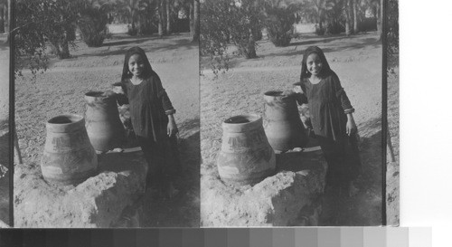 A little Egyptian girl photographed by the water jars provided for the natives on the road between Luxor and Karnak. Egypt