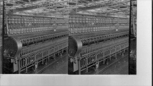 Wet Spinning. The roving being spun into liven yarn - roving comes from two rows of spools - passes through boiling water and is spun on a small bobbin - bobbins seem below small wheels and above round weights. Guelph, Canada