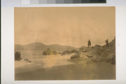 Two photographers on rocks near the ocean or the Golden Gate