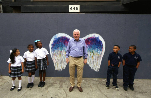 Richard Riordan posing in front of a mural depicting angel wings