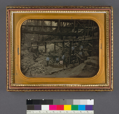 [River bed mining scene with seven miners under a sluice network.]