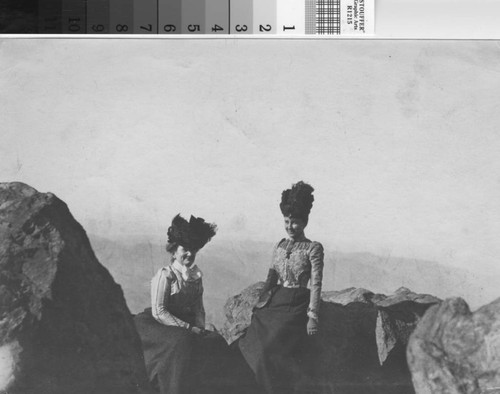 Two women with large upright hats pose at a rock overlook at the top of Mount Tamalpais