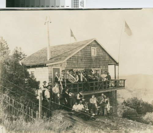 Members with musical instruments standing on and under the deck of the Swiss Club Tell clubhouse