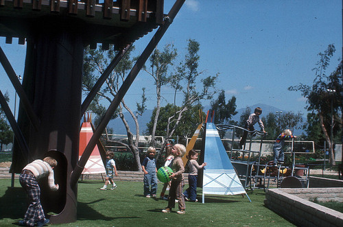 [Children playing on playground with teepees slide]