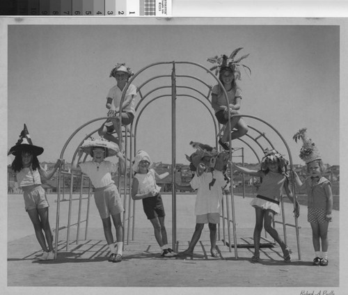 [Children on monkey bars wearing playful hats photograph]