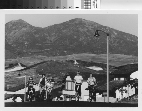 [Family riding bicycles in neighborhood with Saddleback Mountain in background photograph]