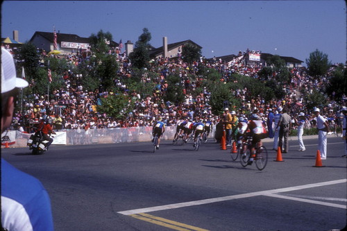 [1984 Olympics Men's Cycling Road Race showing cyclists turning a corner in front of a slope filled with spectators slide]