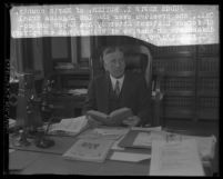Judge Edwin I. Butler with book in hand, sitting at desk with shelves of law books behind him in Los Angeles, Calif., 1929