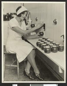 Woman worker filling honey jars from a tank, ca.1930