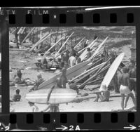 Surfers hanging out, with their boards propped against fence at Malibu Point Beach, Calif., 1966