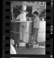 Two boy shoe shiners standing on their boxes to reach a lunch counter in Los Angeles, Calif., 1966