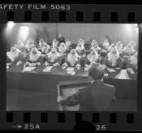 Twenty-four men in Santa suits, at the Sears, Roebuck Company Santa Claus school in Los Angeles, Calif., 1976