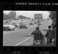 Two men in wheelchair procession on Ventura Freeway with sign reading "RTD is Unfair", Los Angeles, Calif., 1981