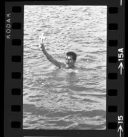 John G. Amarantos holding up wooden cross he recovered from the ocean during Greek Orthodox rite in Long Beach, Calif., 1967