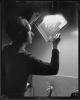 Photographer or technician holding an exposed and developed photographic sheet up to a light source, Los Angeles, 1935