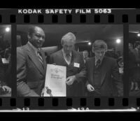 Tom Bradley holds sign for Freedom of Press exhibit while at reception for the event with Otis Chandler and Hugh Hefner. B. 1980