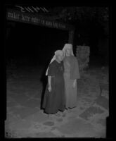 Bishop Nekona and Sister Muriel stand, with eyes closed, in the ruins of the Fountain of the World headquarters, 1958