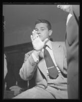 Tom Neal, being questioned in th eoffice of District Attorney S. Ernest Roll, waves hand to deny initiating the fight that landed Franchot Tone in the hospital, 1951