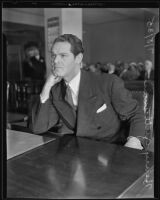 Henry Guttman, accused of theft, leans his chin on his hand as he sits in the courtroom, Los Angeles, 1935