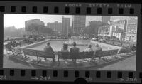 Wide-angle panoramic of people seated on park benches around fountain in Pershing Square, looking south, Los Angeles, Calif., circa 1973