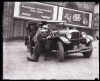 Three plain-clothed police men crouched behind a car aiming their guns, Los Angeles, circa 1925