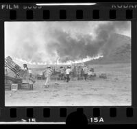 Farm workers moving wooden crates as brush fire descends hill in Halsey Canyon, Calif., 1979