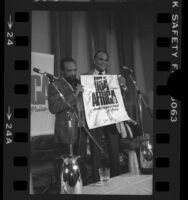 Music producer Quincy Jones and singer Harry Belafonte holding up autographed USA for Africa poster at press conference in Los Angeles, Calif., 1985