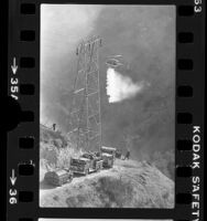 Helicopter dropping water on wildfire as firefighters watch near Porter Ranch, Calif., 1976