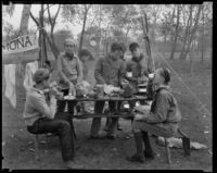 Boy Scouts share a meal at a camping event in a park, circa 1935