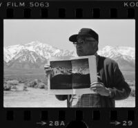 Japanese American man displays book of Ansel Adams' Manzanar photographs