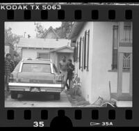 Police officer escorting hand-cuffed man identified as Norman Young from home in South Los Angeles, Calif., 1986