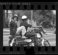 Clown getting a ride from a motorcycle policeman in Los Angeles, Calif., 1976